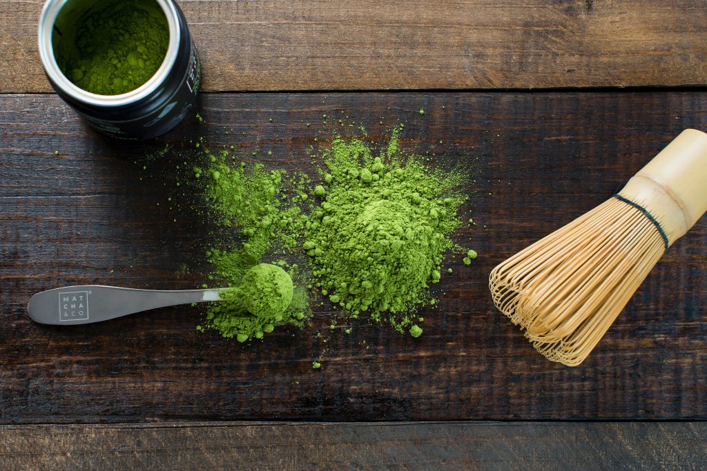 Matcha powder with whisk on wooden table-min